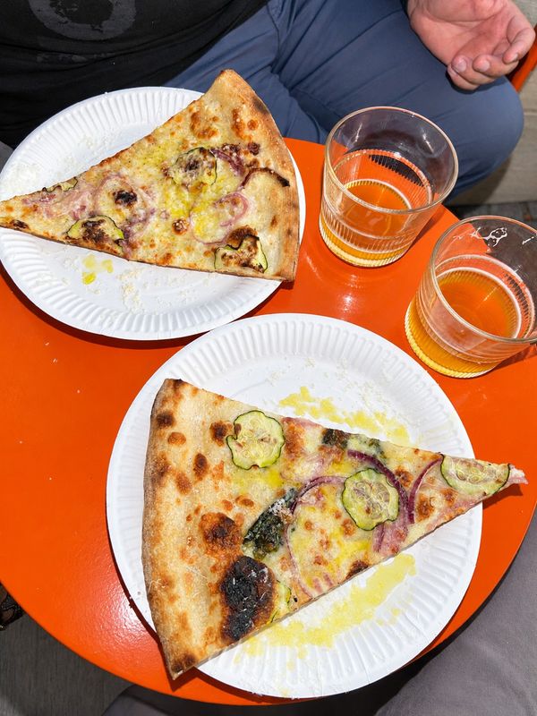 Två pizzaslices på papptallrikar med öl på ett orange bord, Bennys Slice Shop
