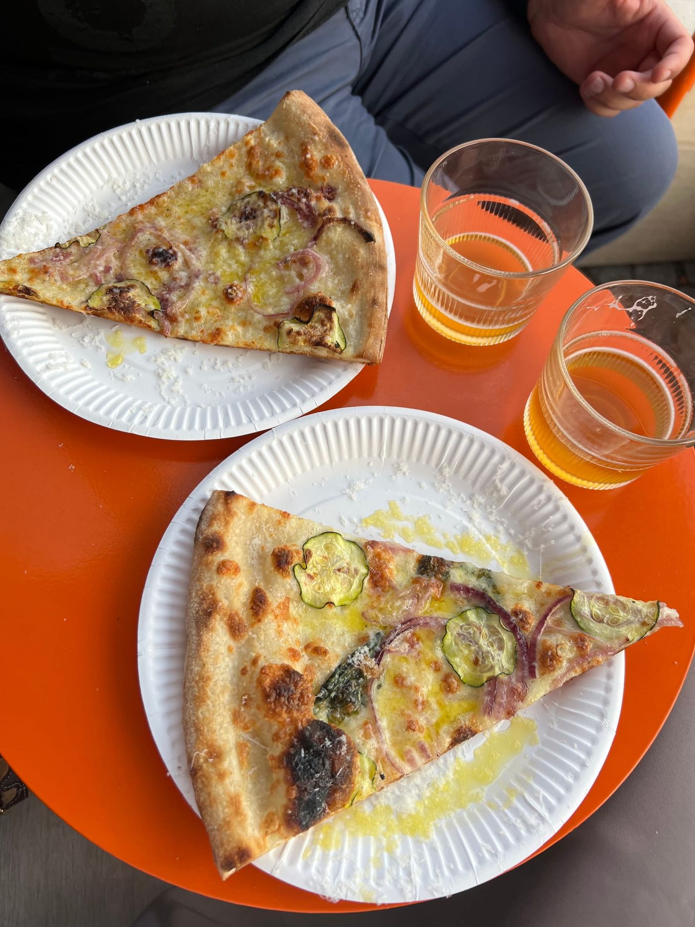 Två pizzaslices på papptallrikar med öl på ett orange bord, Bennys Slice Shop