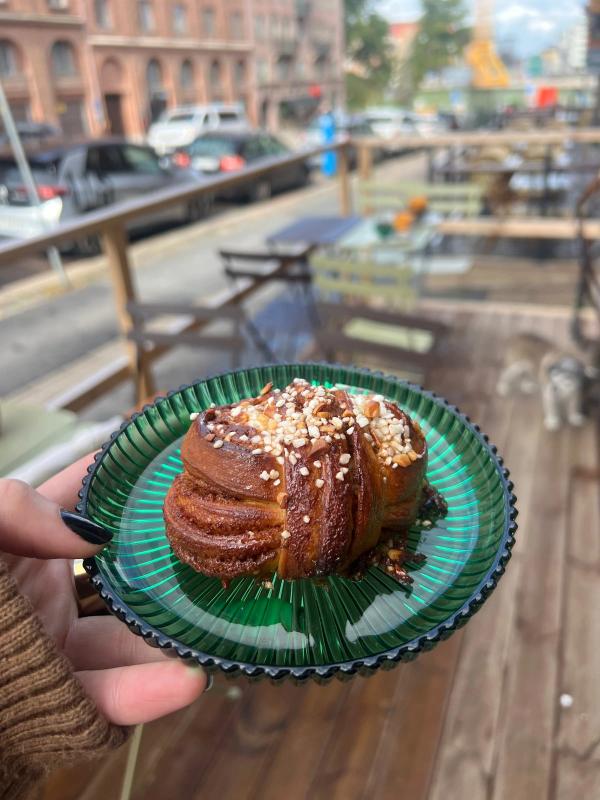 Kanelbulle med pärlsocker på grönt glasfat framför uteserveringen, Sol