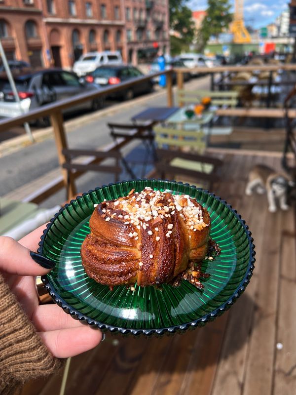 Kanelbulle med pärlsocker på grönt glasfat framför uteserveringen, Sol