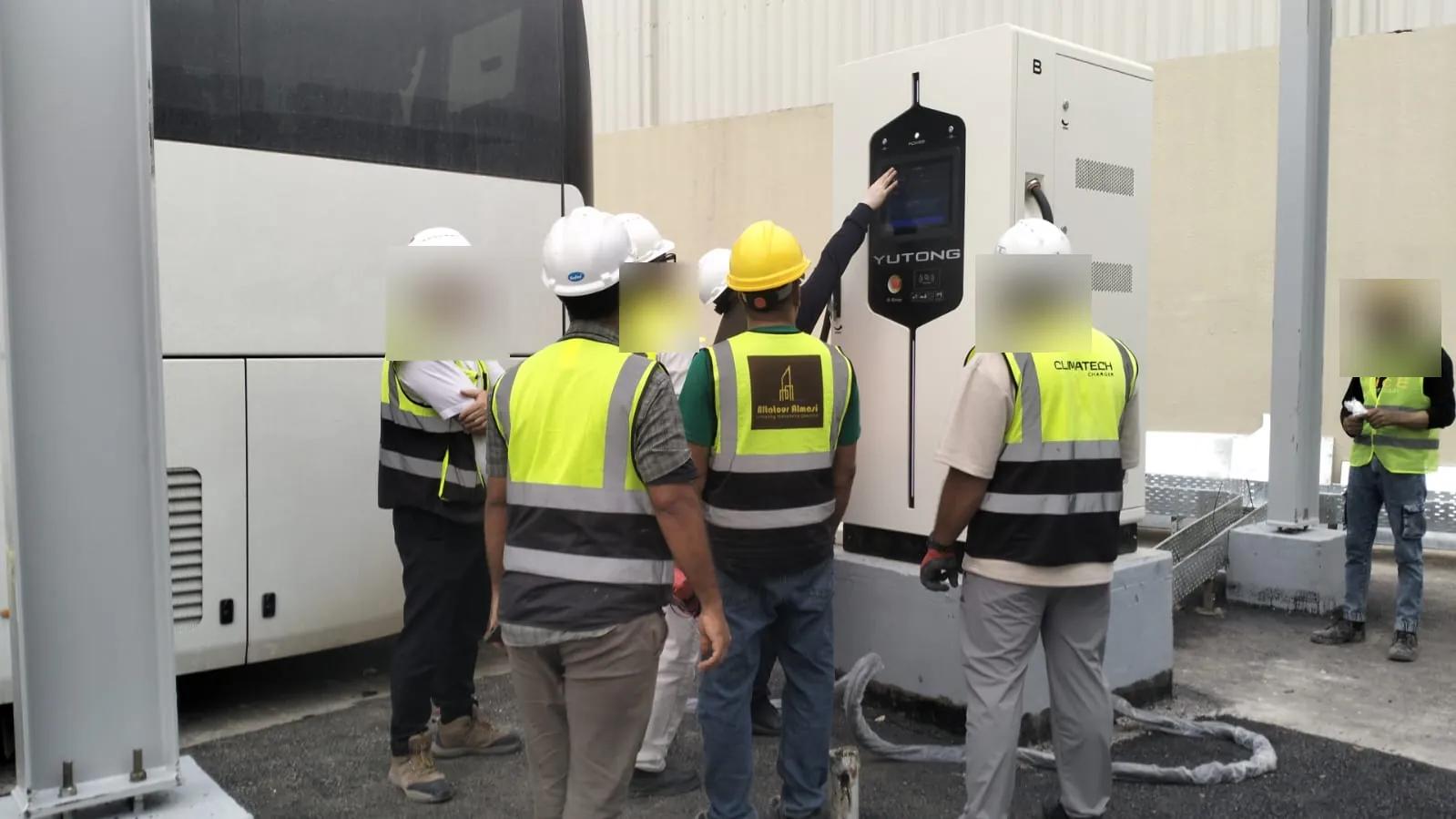 فريق كلايمتك وفريق العميل بسترات السلامة عند شاحن Yutong DC بجانب حافلة كهربائية