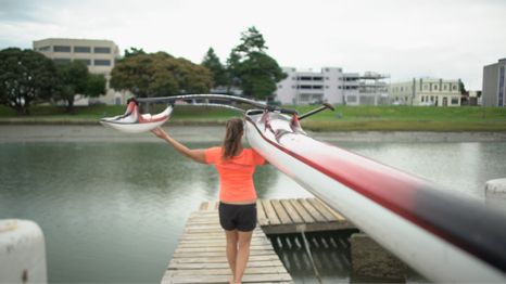 A woman carrying a rowing boat on her shoulder facing a river