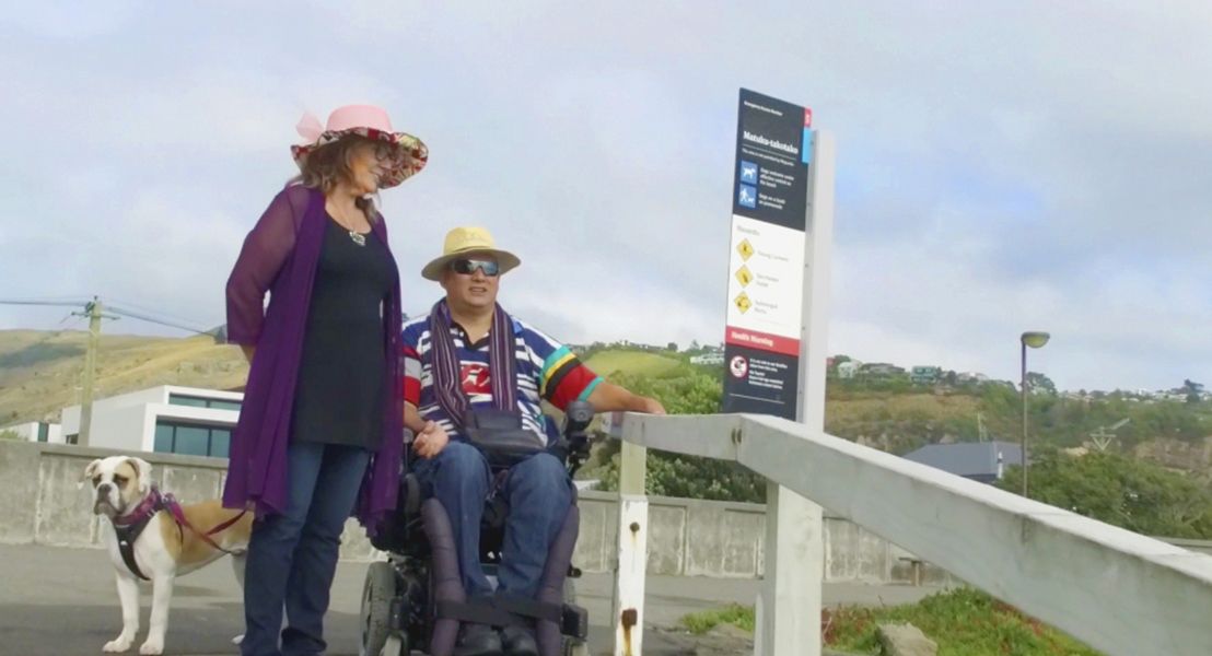 A woman standing next to a man in a wheelchair at the beach