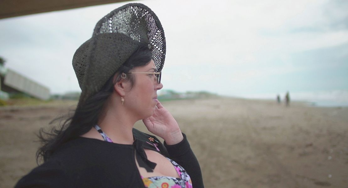A woman in a sunhat standing on a beach staring out at the water