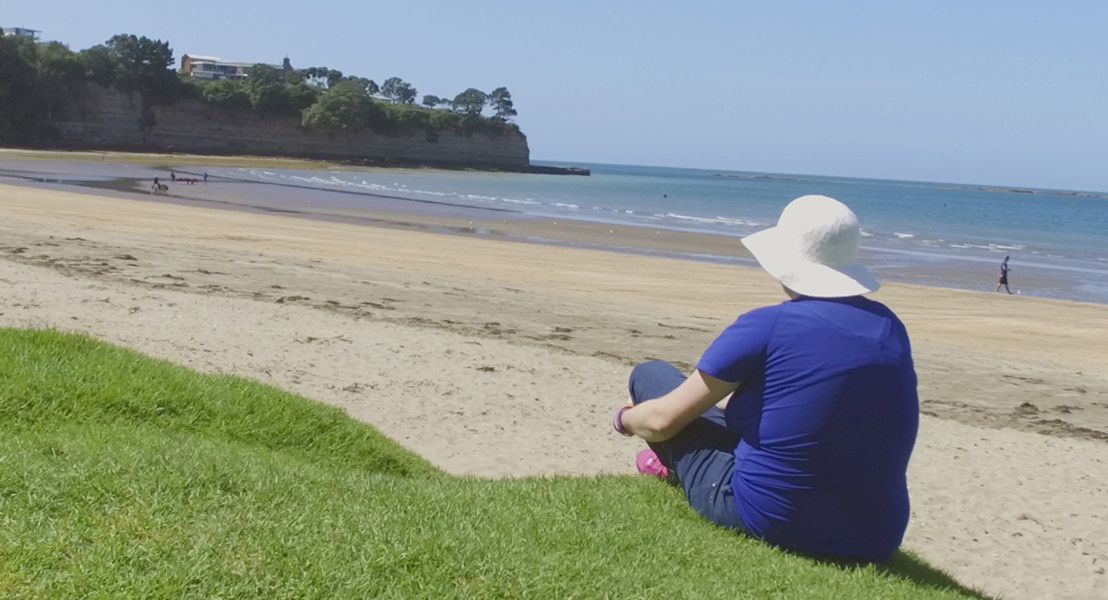 A woman sitting on a hill staring out at a beach