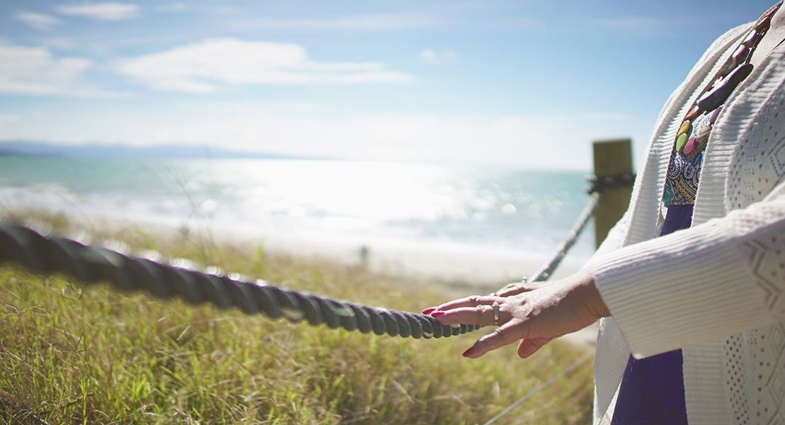 A person's hand on a rope handrail leading towards a beach
