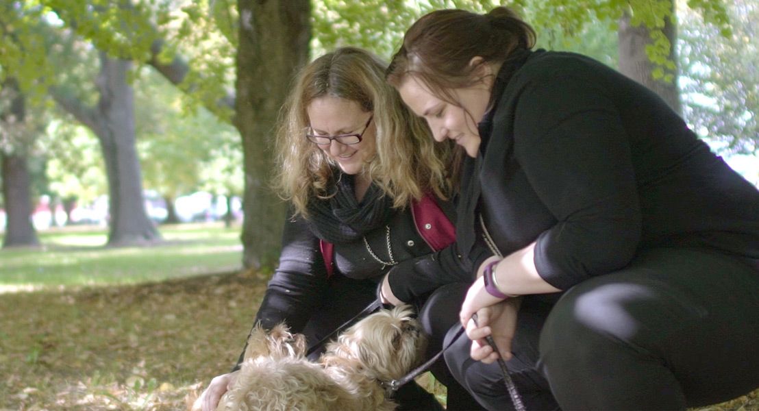 Two women crouching down to pat a dog