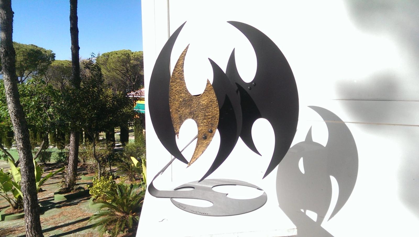 Black painted iron flame-form sculpture with a hammered brass core, outdoors
