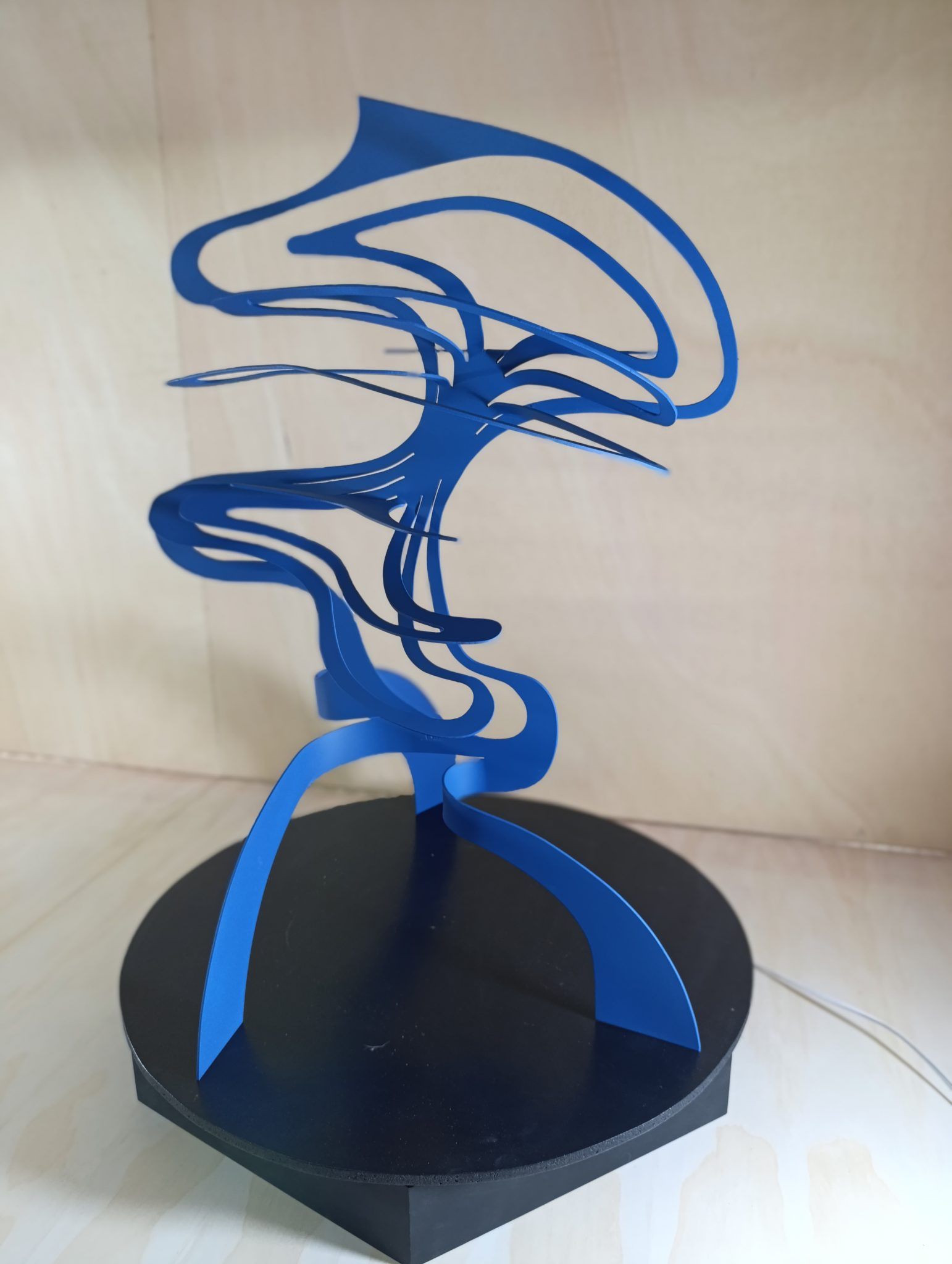 Blue painted iron ribbon sculpture spiraling upward from a black base