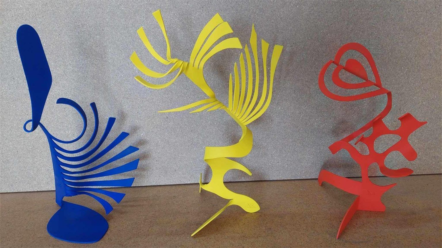 Three painted iron sculptures in blue, yellow, and red on a studio backdrop