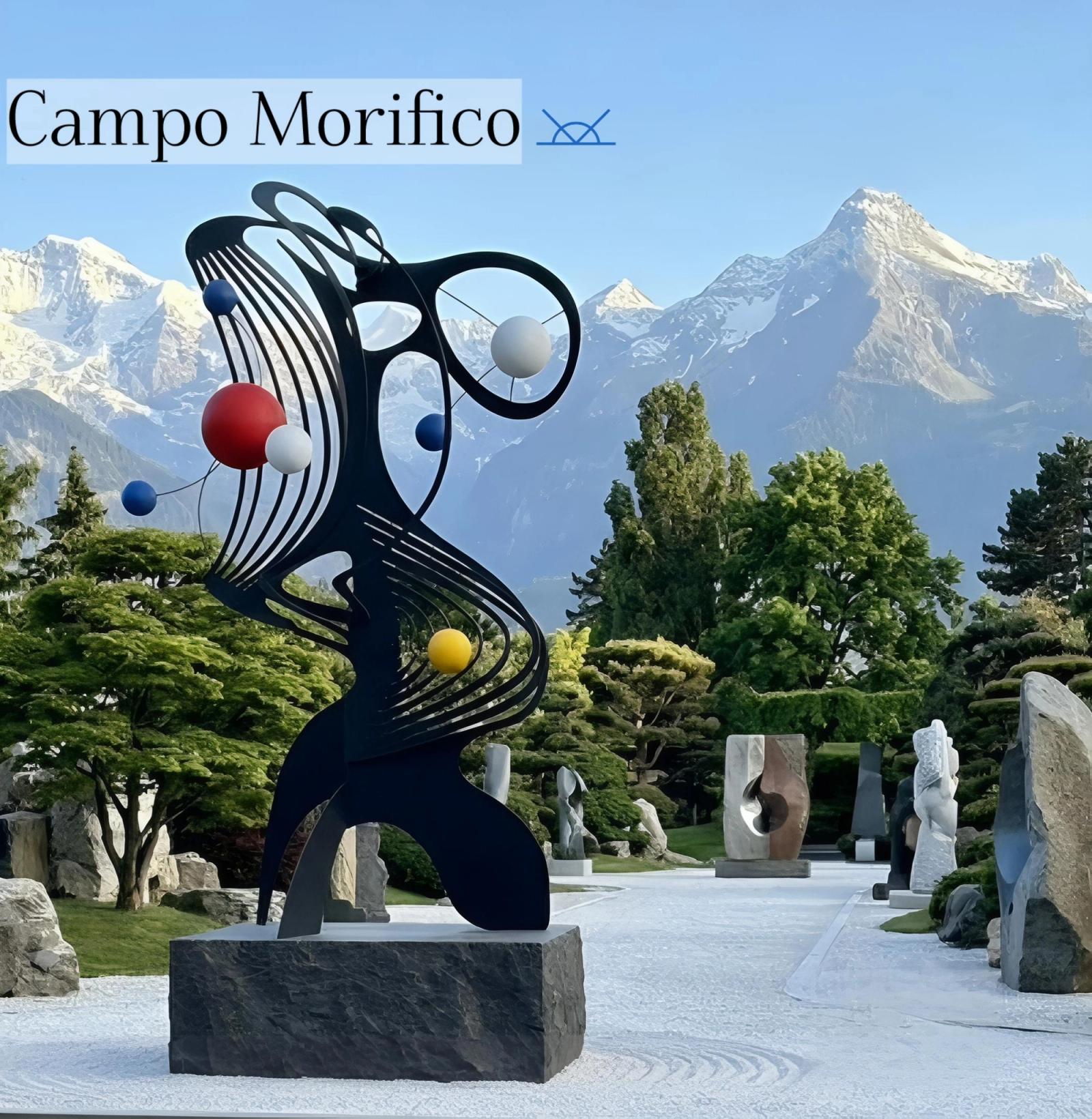 “Campo Morifico - Genesis” – abstract black painted steel sculpture with colorful spheres, displayed in a sculpture garden with dramatic alpine mountains in the background.
