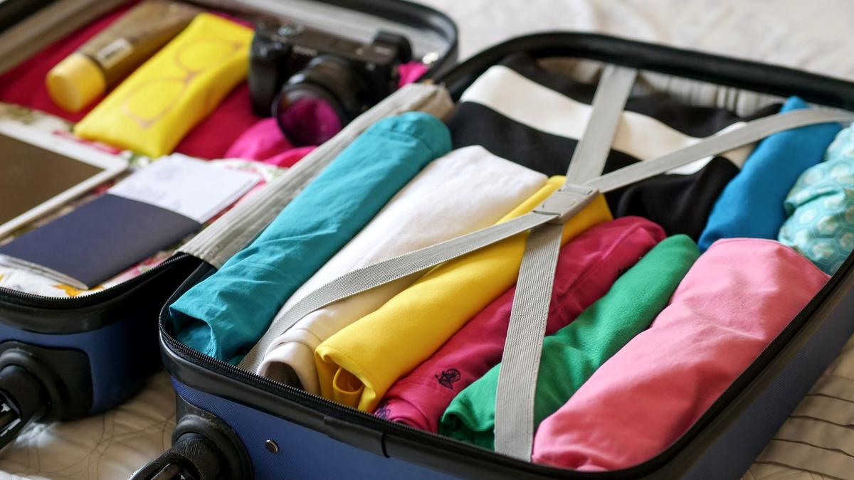 A clamshell travel backpack opened flat and packed with rolled clothes and packing cubes