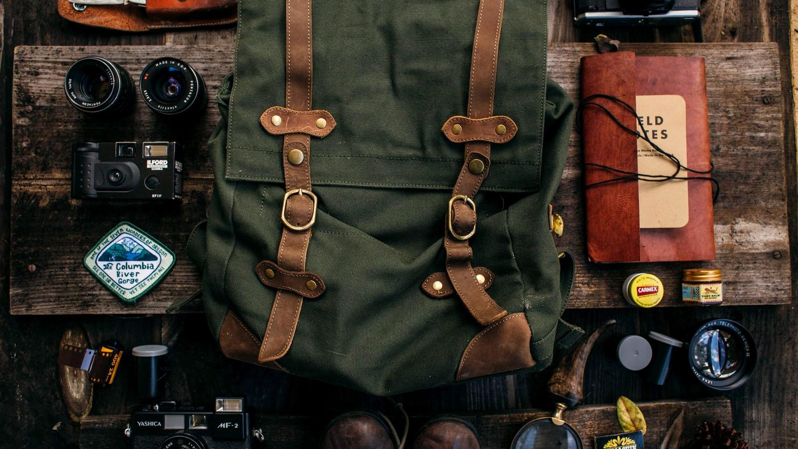 Travel gear flat lay with a canvas backpack, boots, camera, and folded clothes on a table