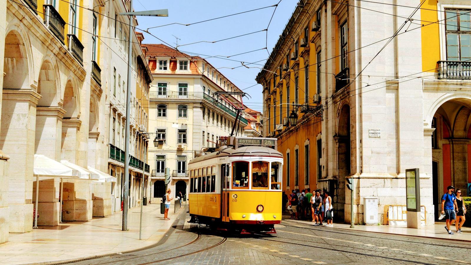 A yellow tram climbing a tiled, cobbled street in Lisbon's Alfama district