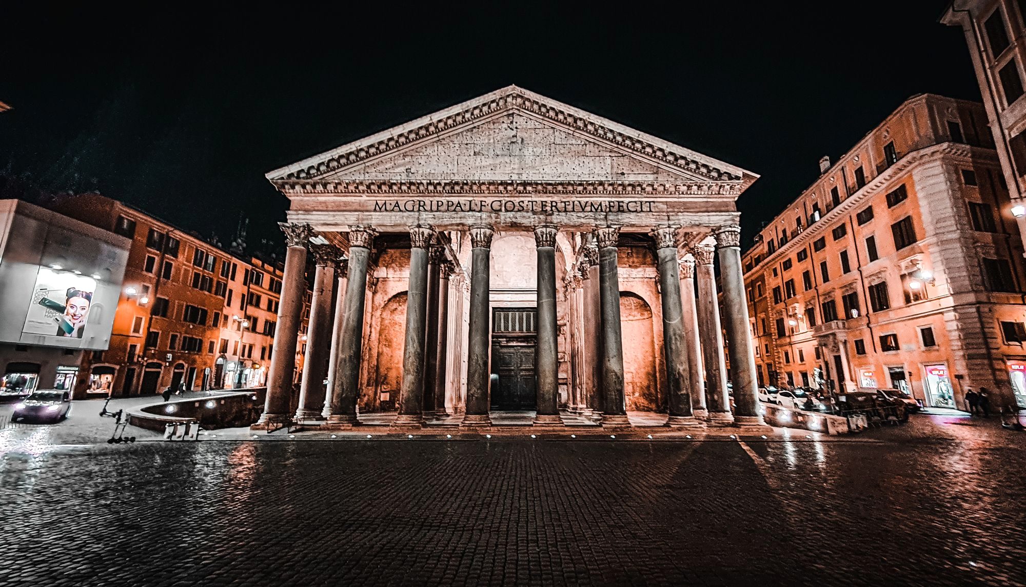 The floodlit Pantheon facade at night above a wet cobbled piazza in central Rome