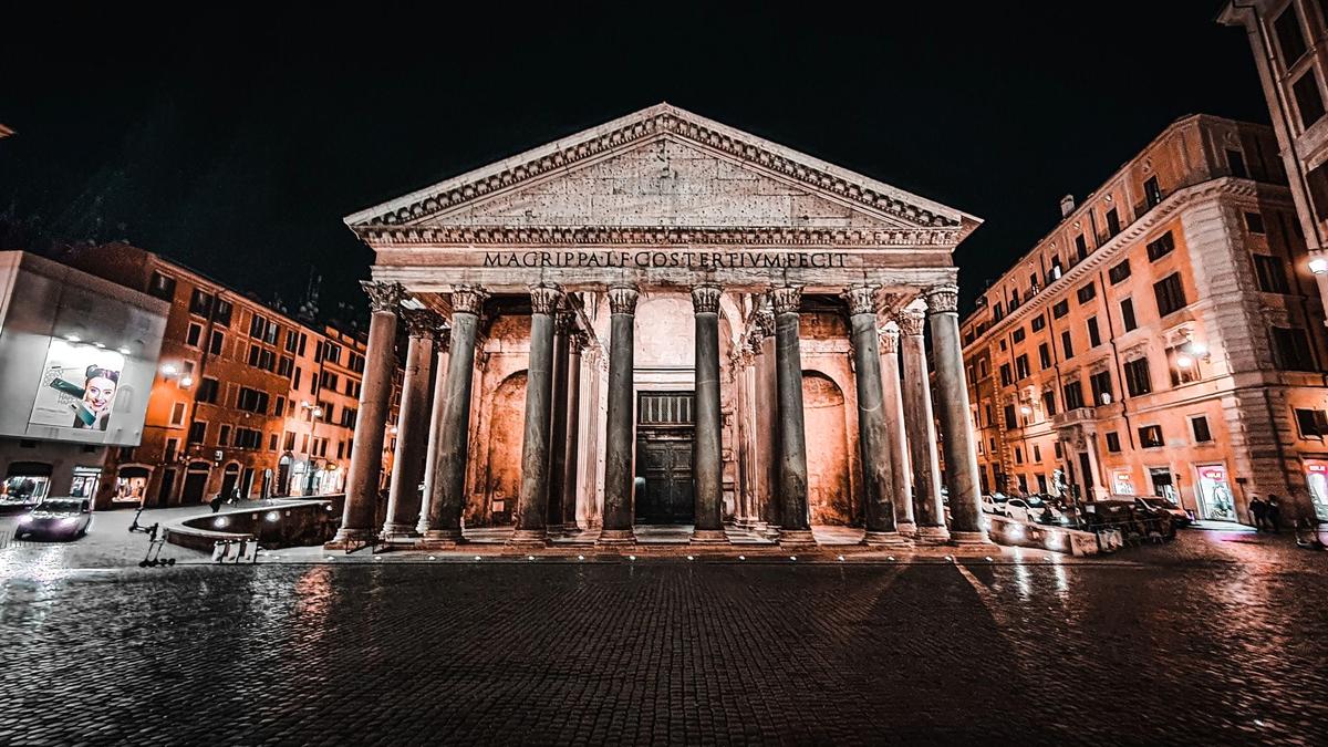 The floodlit Pantheon facade at night above a wet cobbled piazza in central Rome