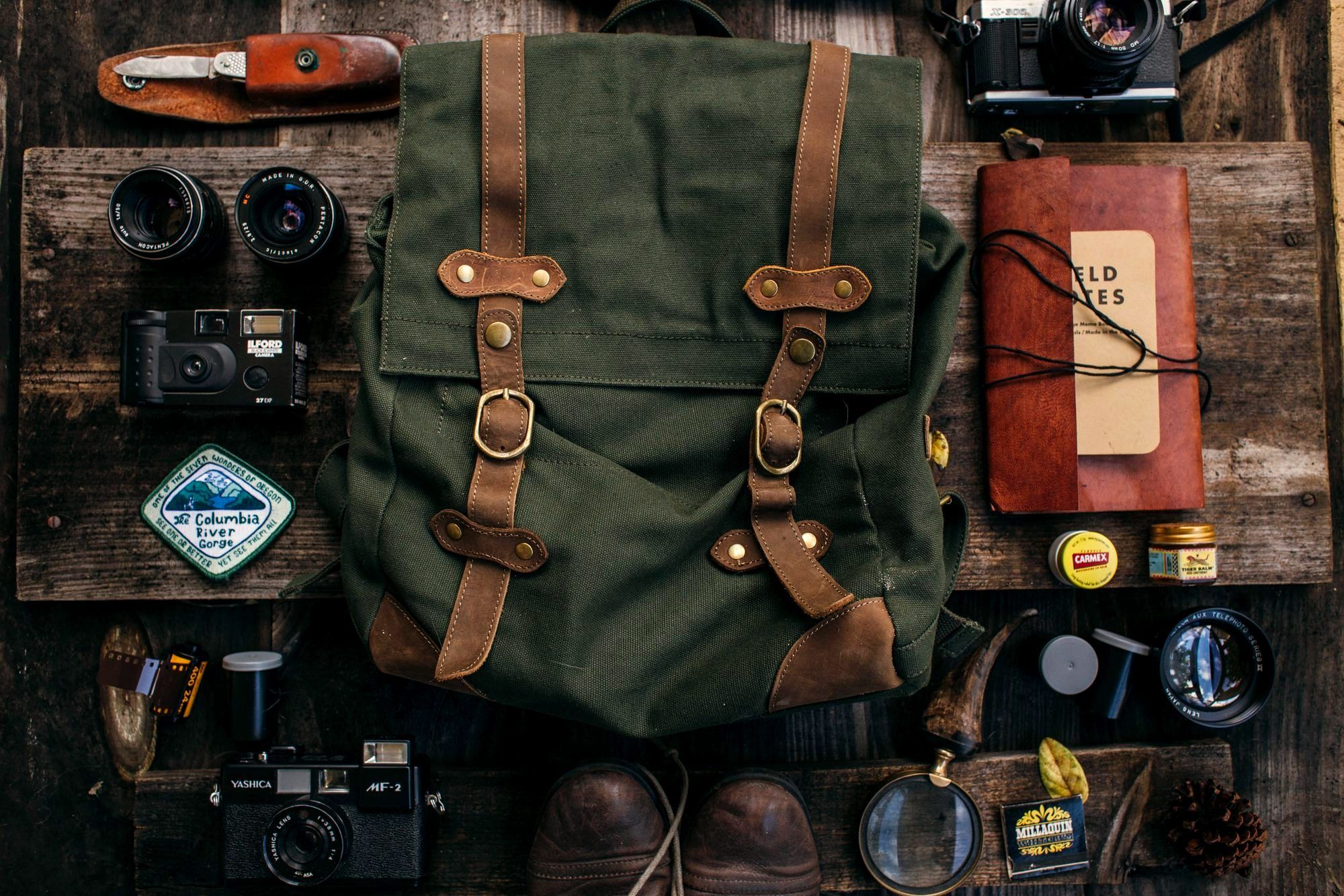 Travel gear flat lay with a canvas backpack, boots, camera, and folded clothes on a table