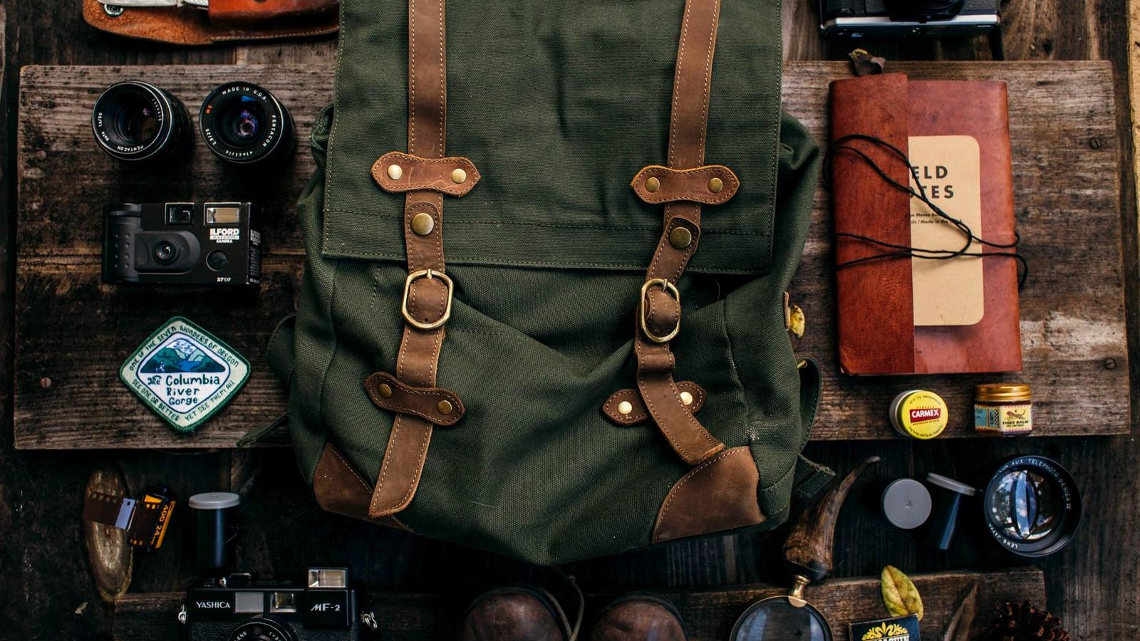 Travel gear flat lay with a canvas backpack, boots, camera, and folded clothes on a table