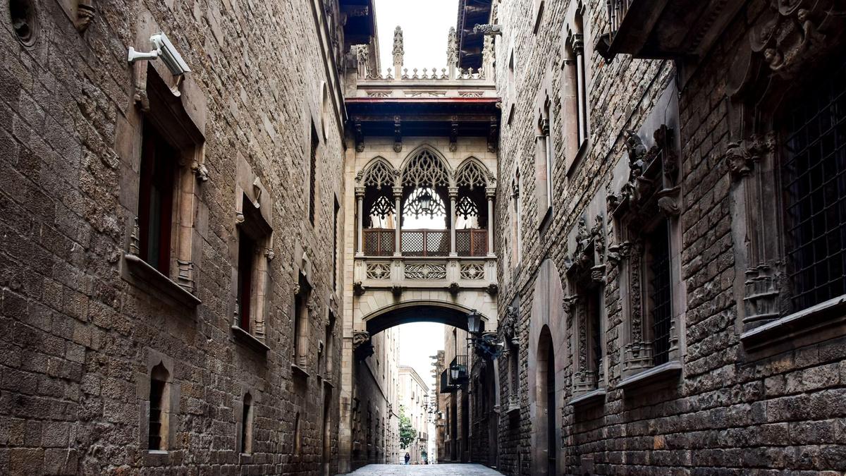 A narrow medieval stone alley in Barcelona's Gothic Quarter with iron balconies