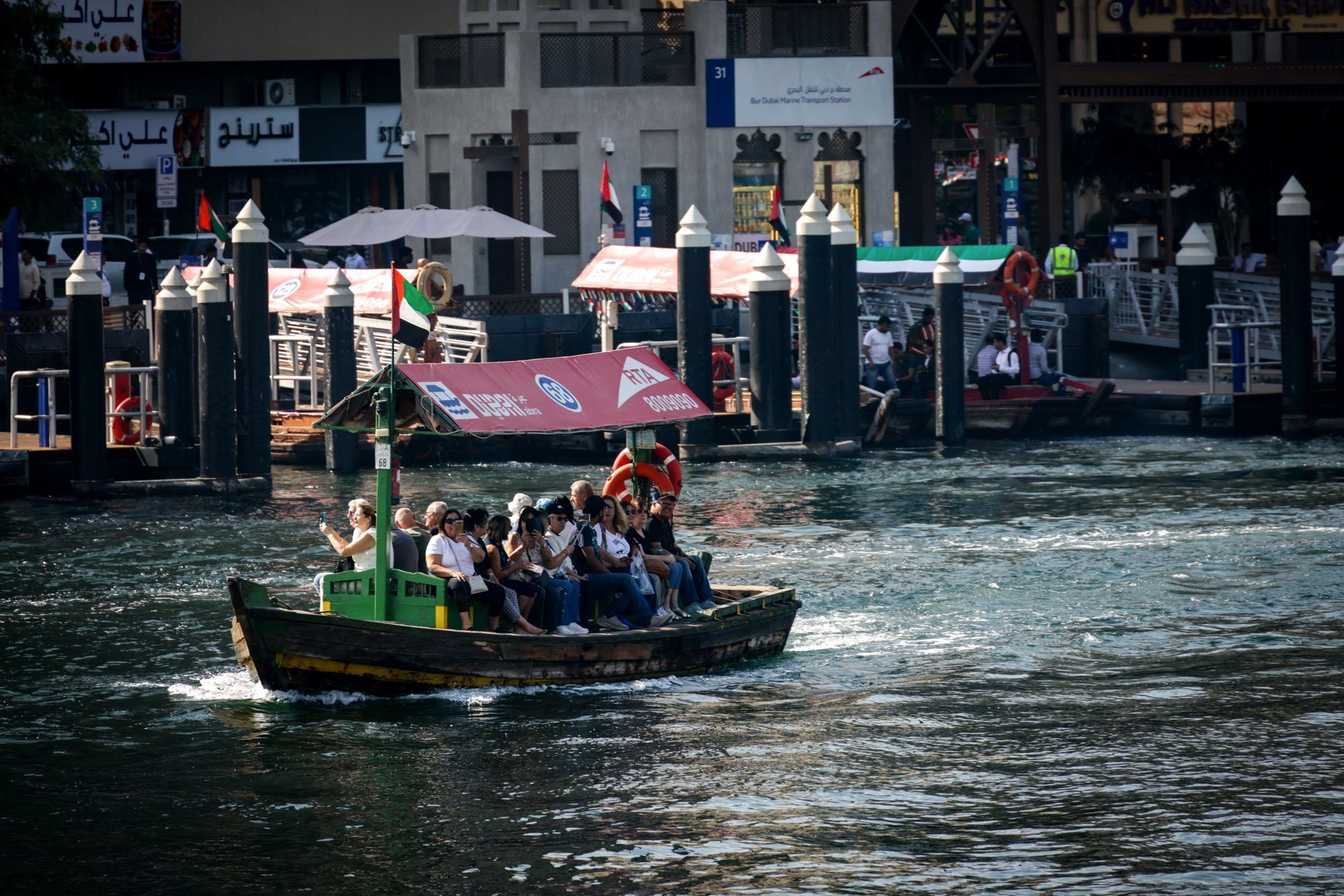 A traditional wooden abra water taxi crossing Dubai Creek with old buildings behind