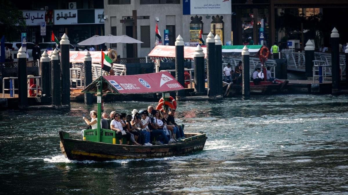 A traditional wooden abra water taxi crossing Dubai Creek with old buildings behind