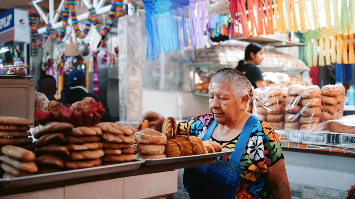 A giant crisp tlayuda topped with beans, quesillo, and grilled meat at a Oaxaca market stall