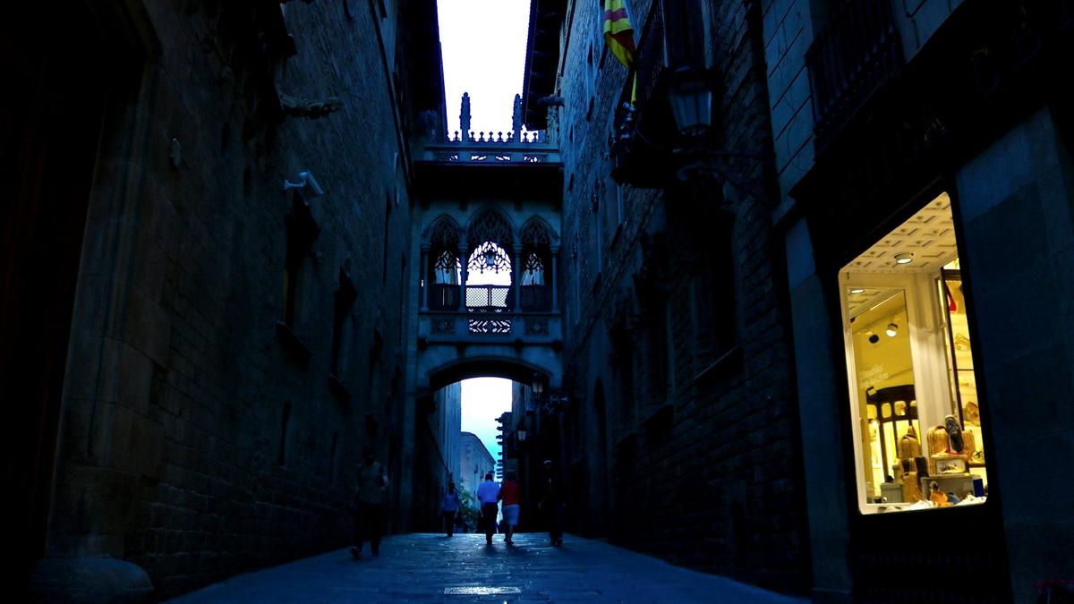 A narrow medieval stone alley in Barcelona's Gothic Quarter with iron balconies