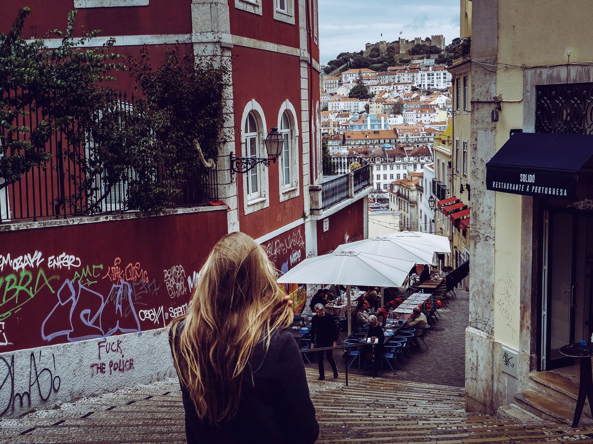 A narrow, steeply climbing alley in Lisbon's Alfama lined with azulejo tiles and iron balconies