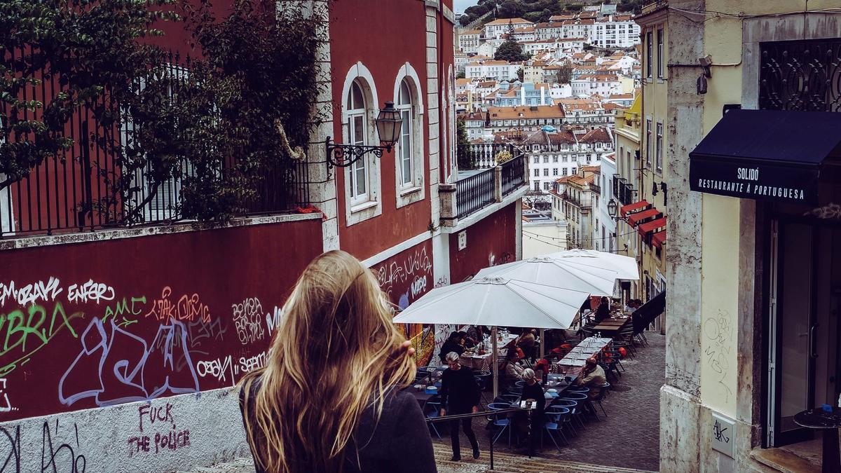 A narrow, steeply climbing alley in Lisbon's Alfama lined with azulejo tiles and iron balconies