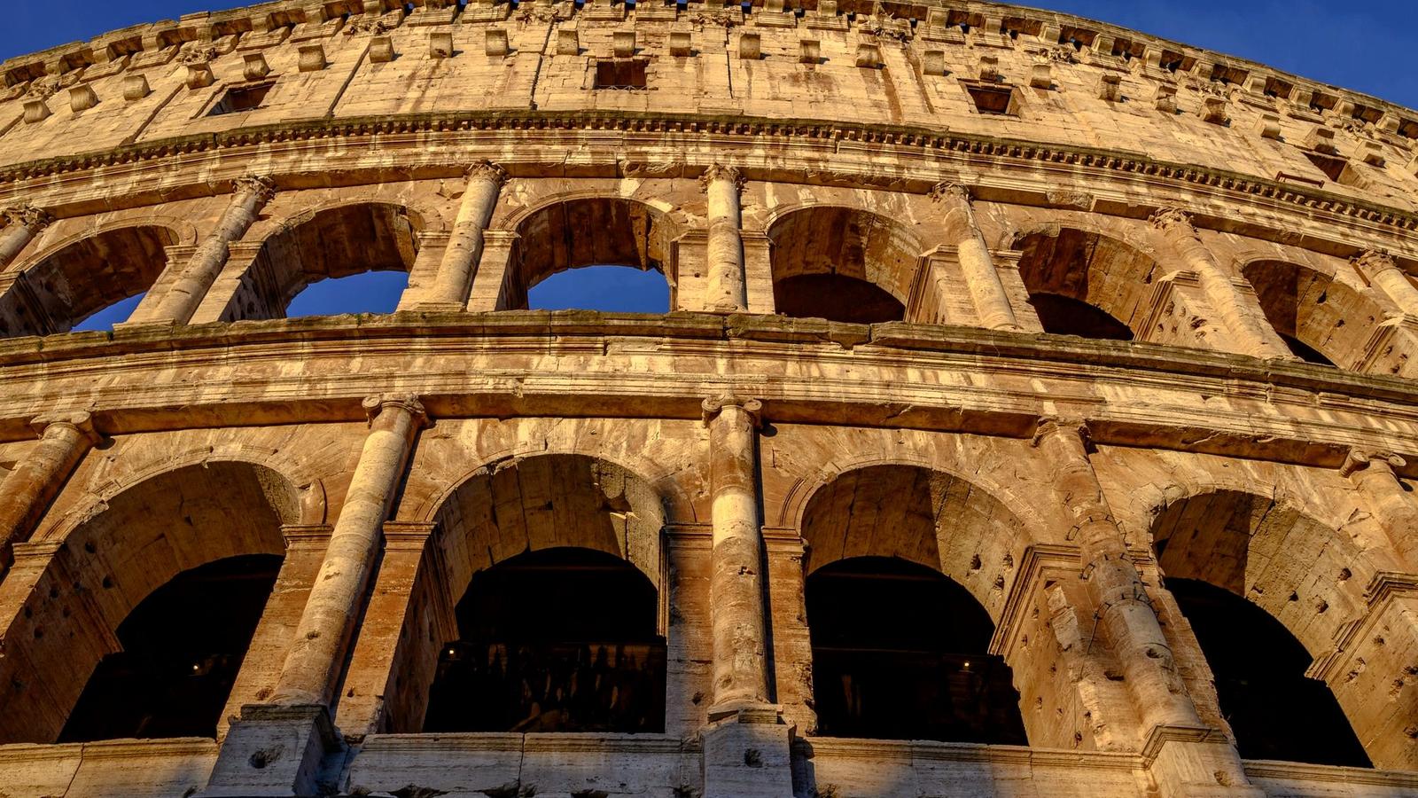 The Colosseum in Rome glowing gold against a deep blue sky at sunset