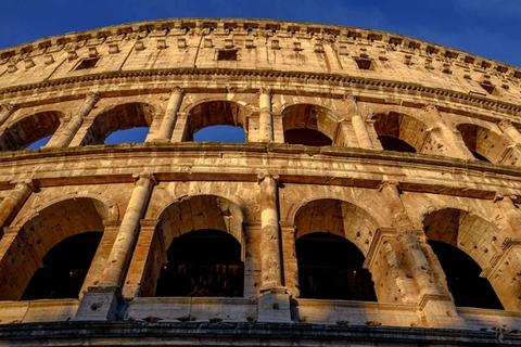 The Colosseum in Rome glowing gold against a deep blue sky at sunset
