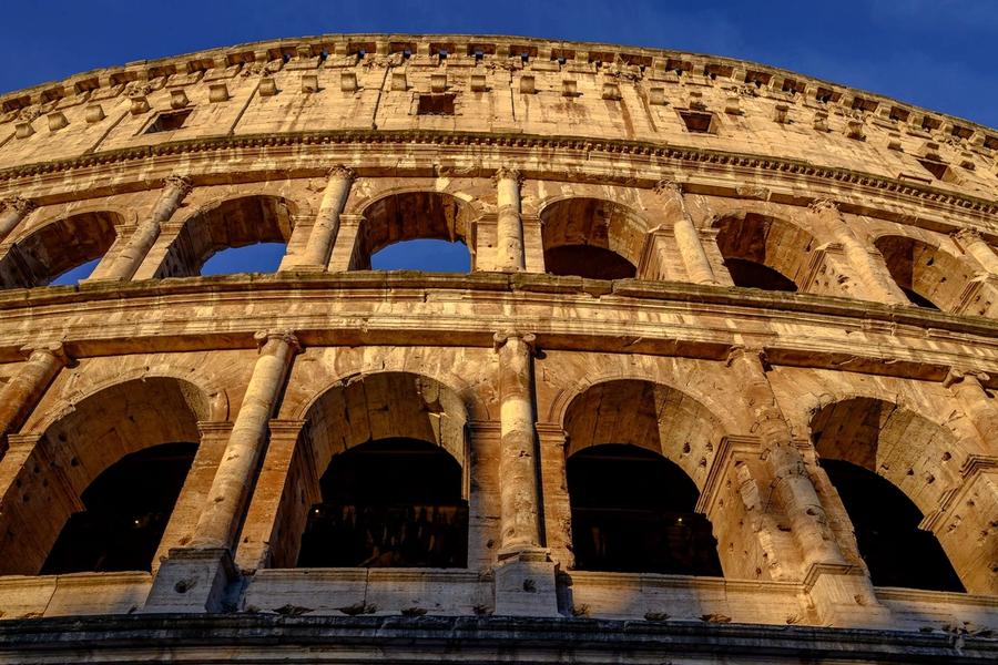 The Colosseum in Rome glowing gold against a deep blue sky at sunset