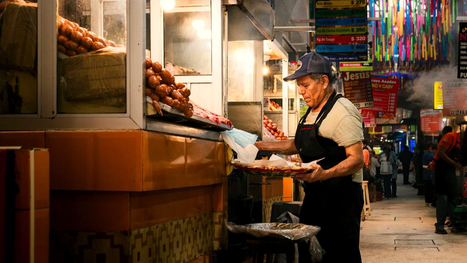 A charcoal-grilled tlayuda being prepared at a busy Oaxaca market stall