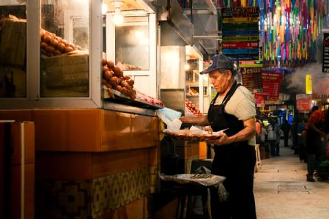 A charcoal-grilled tlayuda being prepared at a busy Oaxaca market stall