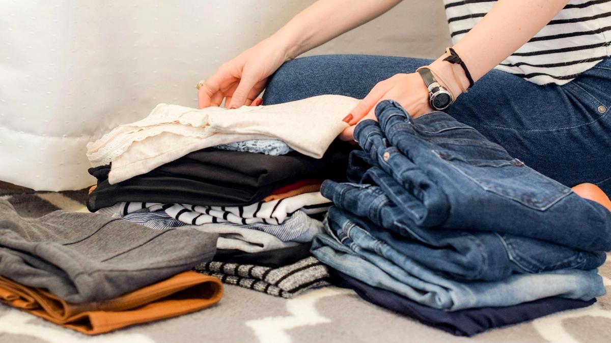 Flat lay of a minimalist capsule travel wardrobe with merino shirts, socks, and a rain shell