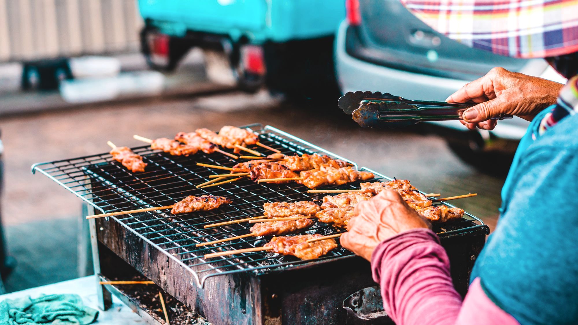 Charcoal-grilled moo ping pork skewers on a Bangkok street cart with a bag of sticky rice