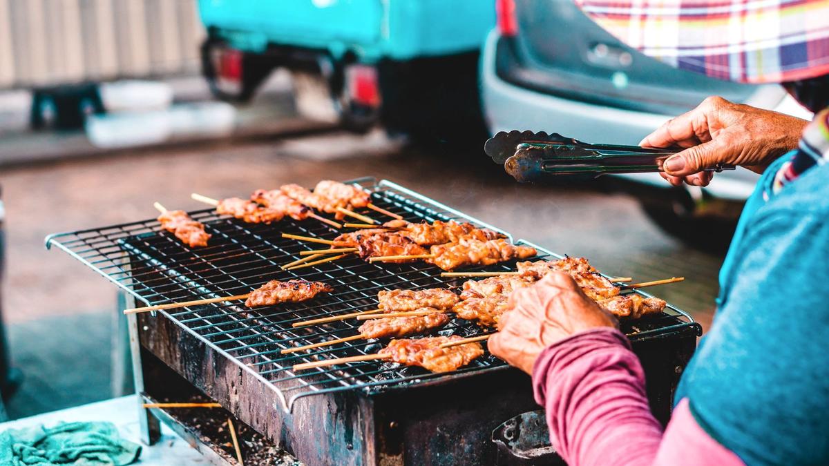 Charcoal-grilled moo ping pork skewers on a Bangkok street cart with a bag of sticky rice