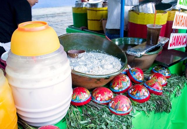 A charcoal-grilled tlayuda being prepared at a busy Oaxaca market stall
