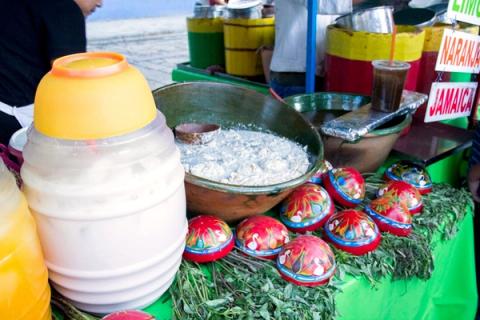 A charcoal-grilled tlayuda being prepared at a busy Oaxaca market stall