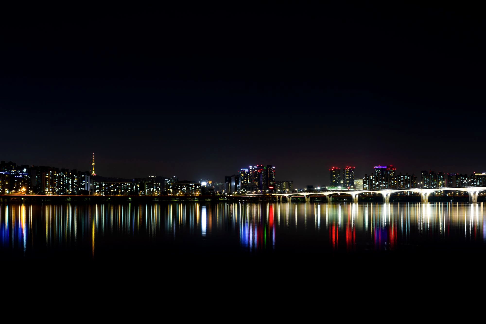 People relaxing on mats along the Han River at Yeouido Park as Seoul lights up at night