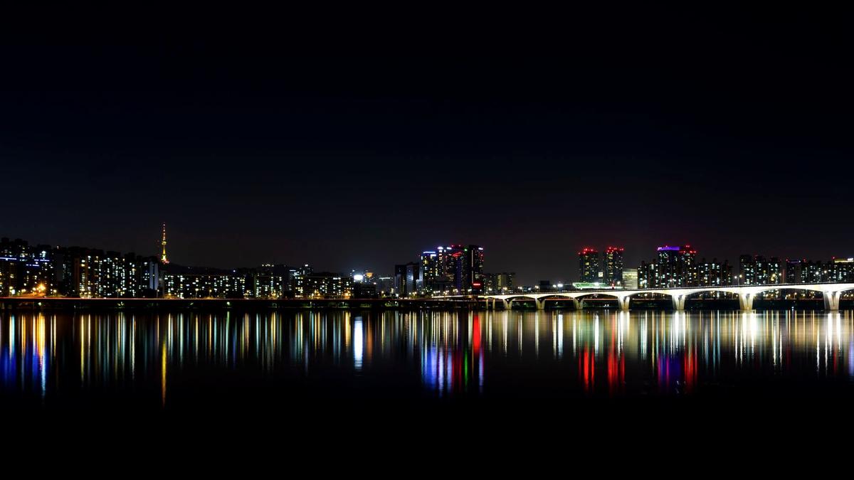 People relaxing on mats along the Han River at Yeouido Park as Seoul lights up at night