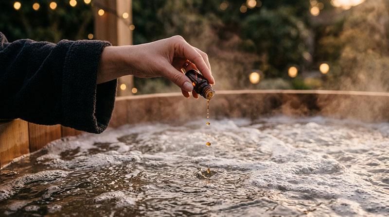 Hand som tillsätter några droppar spadoft i ångande spabadsvatten