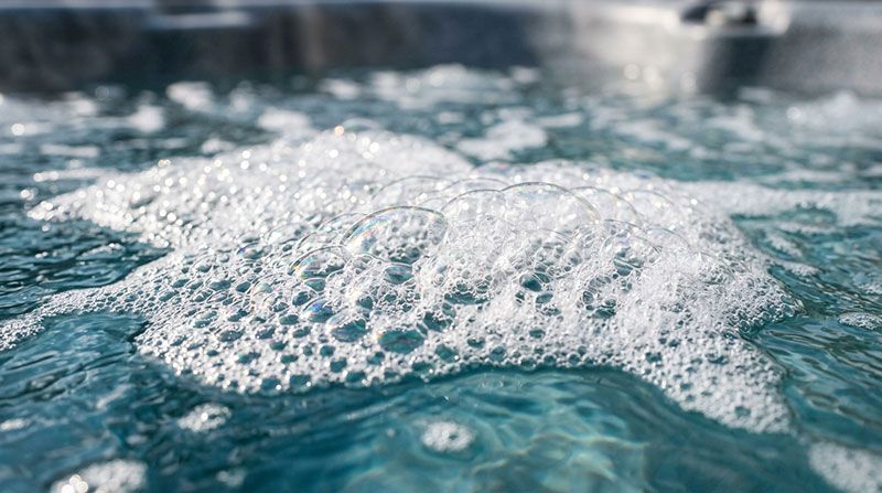 Närbild på vitt skum med fina bubblor på spabadets vattenyta