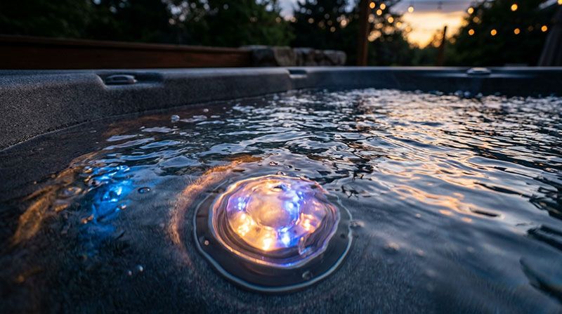 Flerfärgad LED-belysning lyser under vattenytan i spabad vid solnedgång