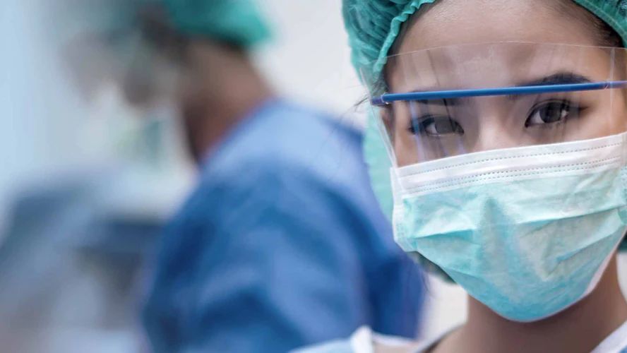 Healthcare worker wearing a surgical mask, cap, and protective glasses