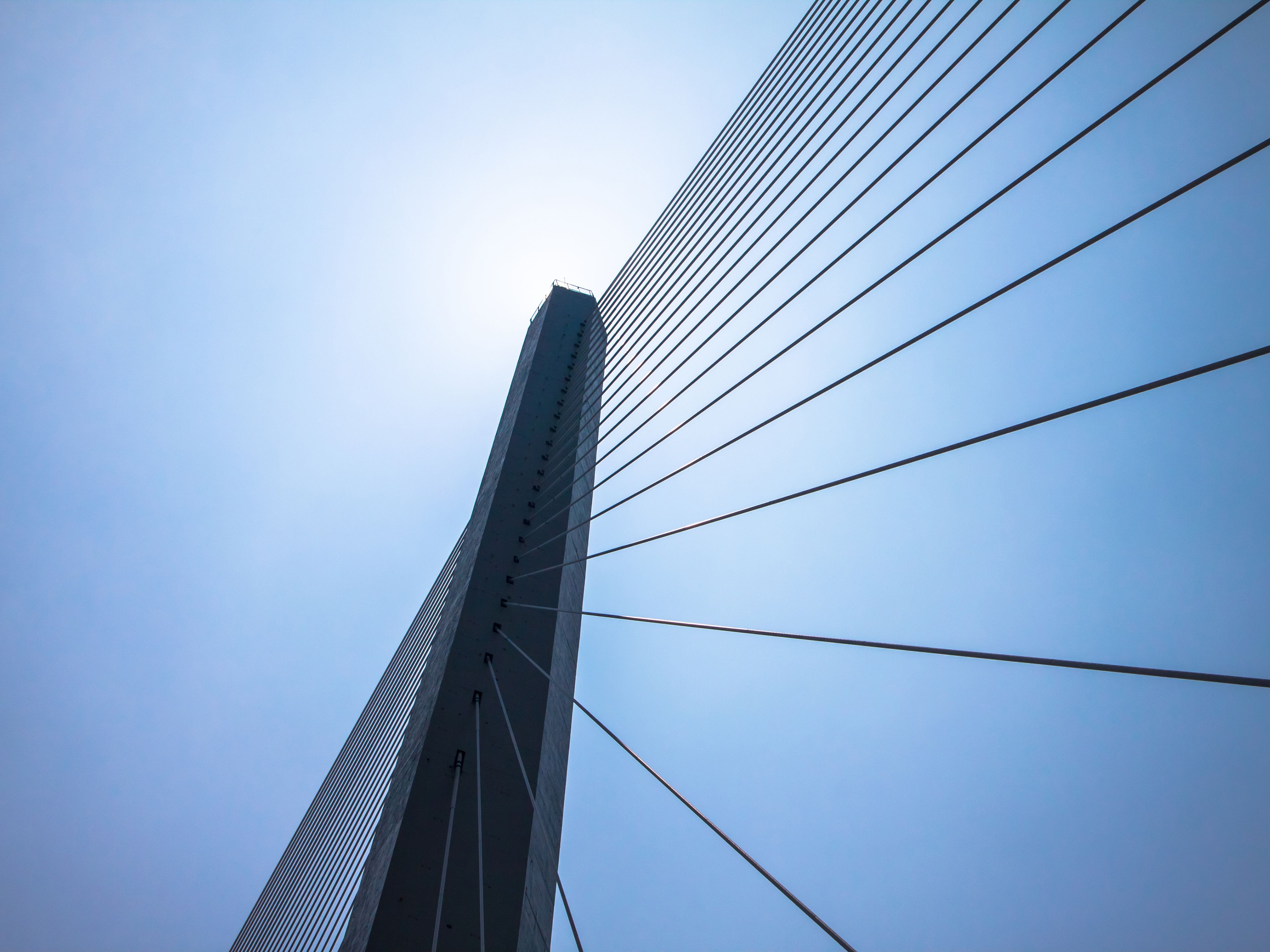 Cable-stayed bridge tower and suspension cables viewed from below against a clear sky, representing modern civil engineering