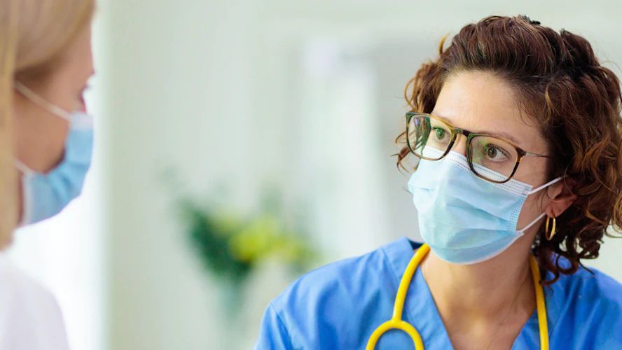 Two healthcare workers wearing surgical masks and stethoscopes in a clinical setting