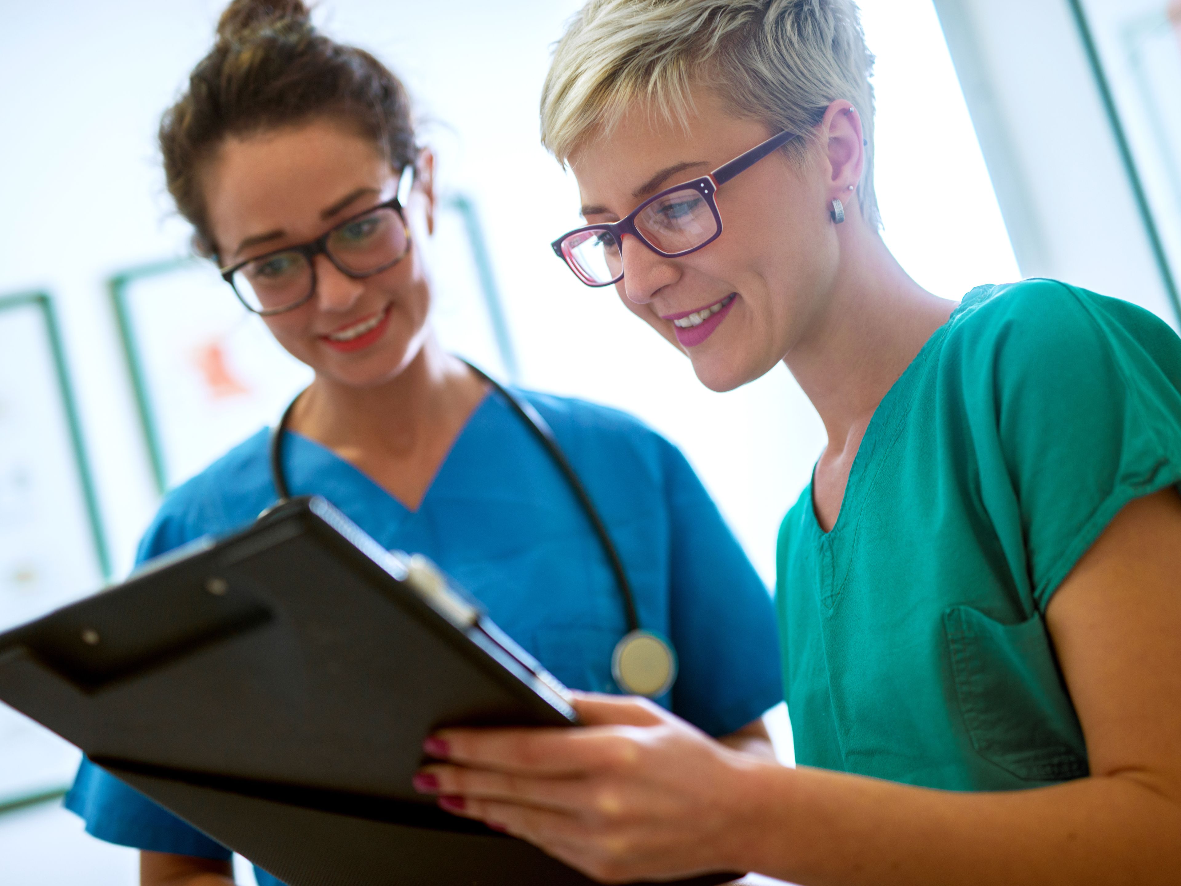 Two nurses in scrubs reviewing a patient chart together in a clinical setting