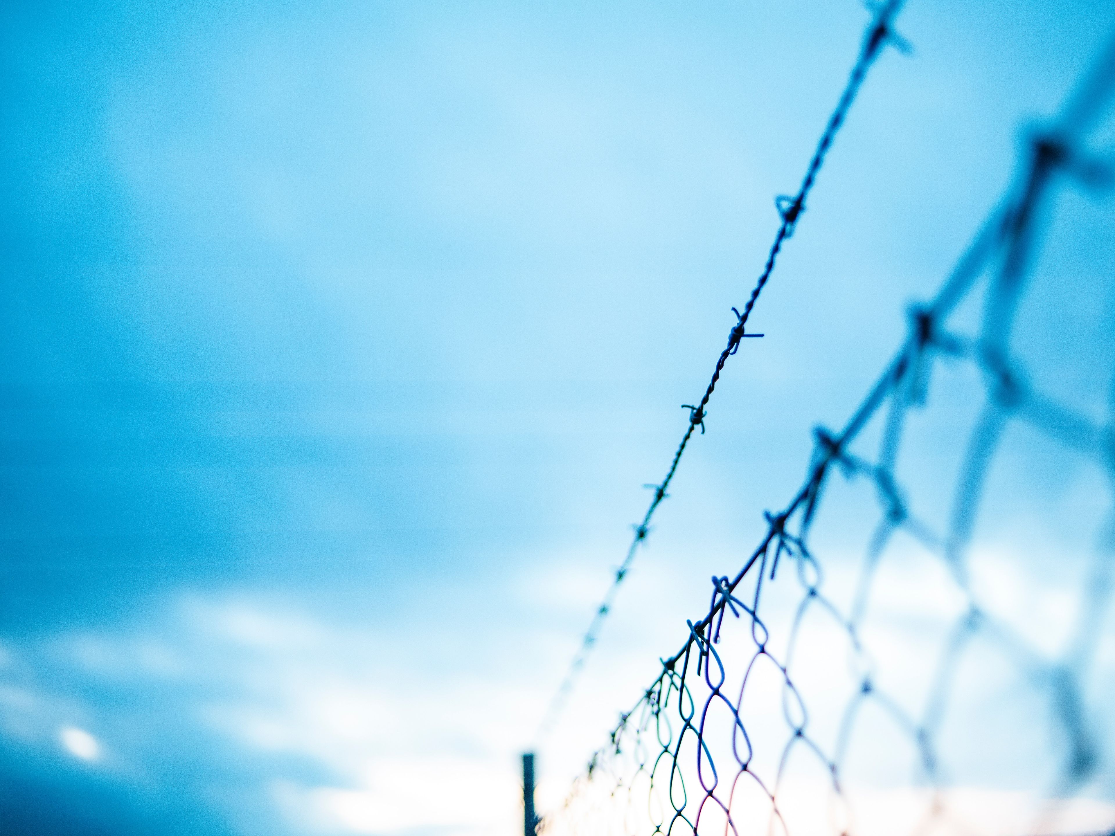 Chain-link fence topped with barbed wire against a moody blue sky, evoking themes of criminal justice and defense