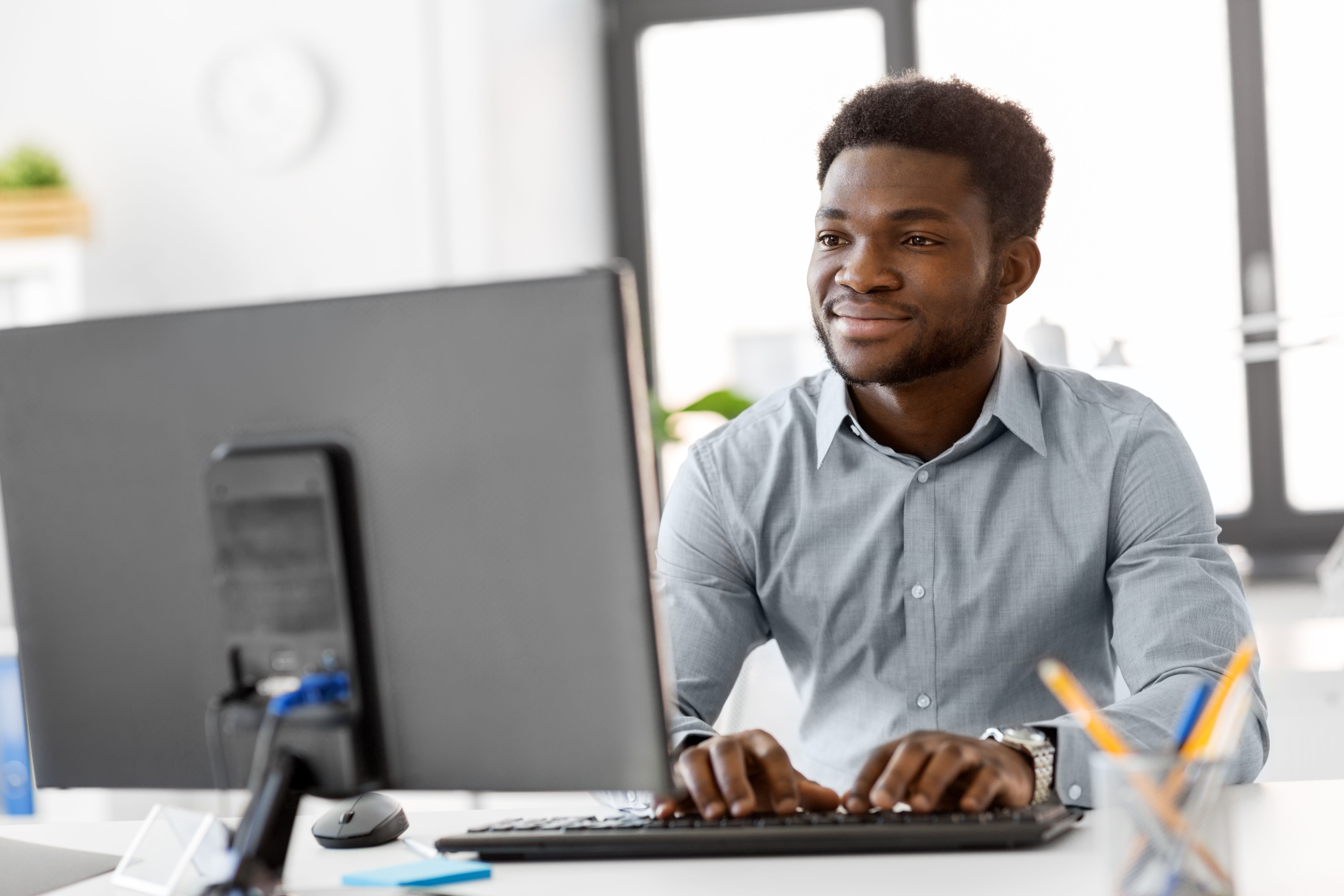 Developer smiling while typing on a desktop keyboard at a bright modern office workspace